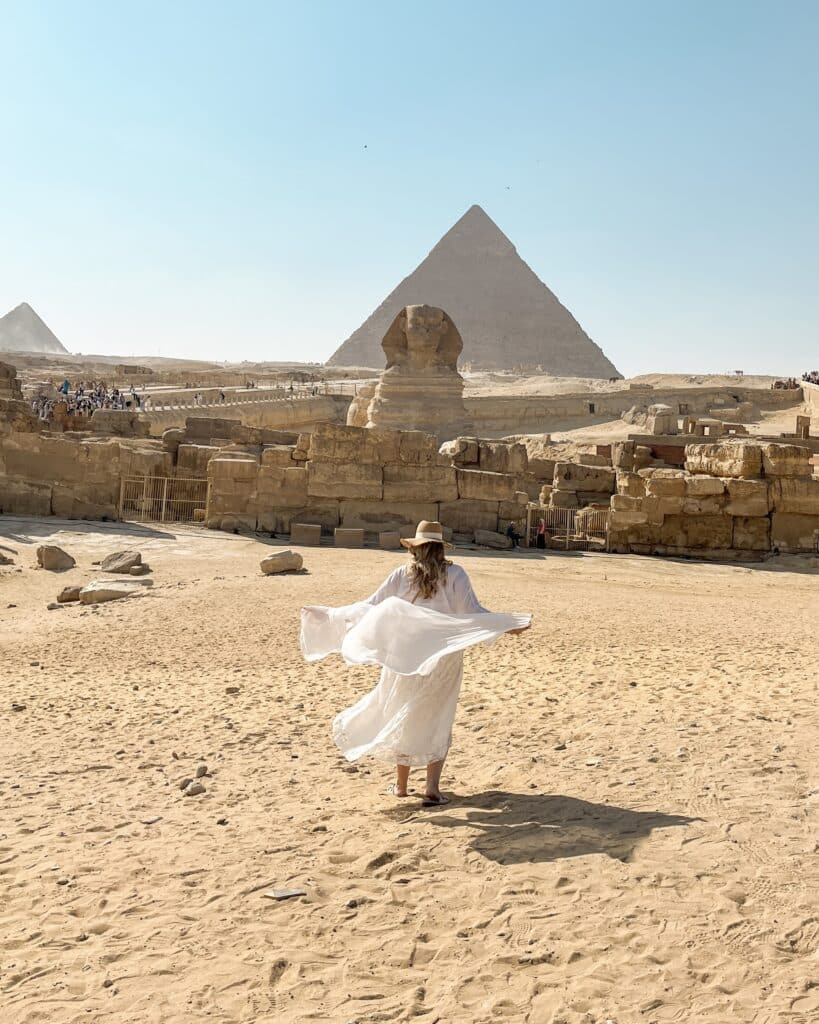 woman walking in front of the sphinx and pyramids of giza egypt